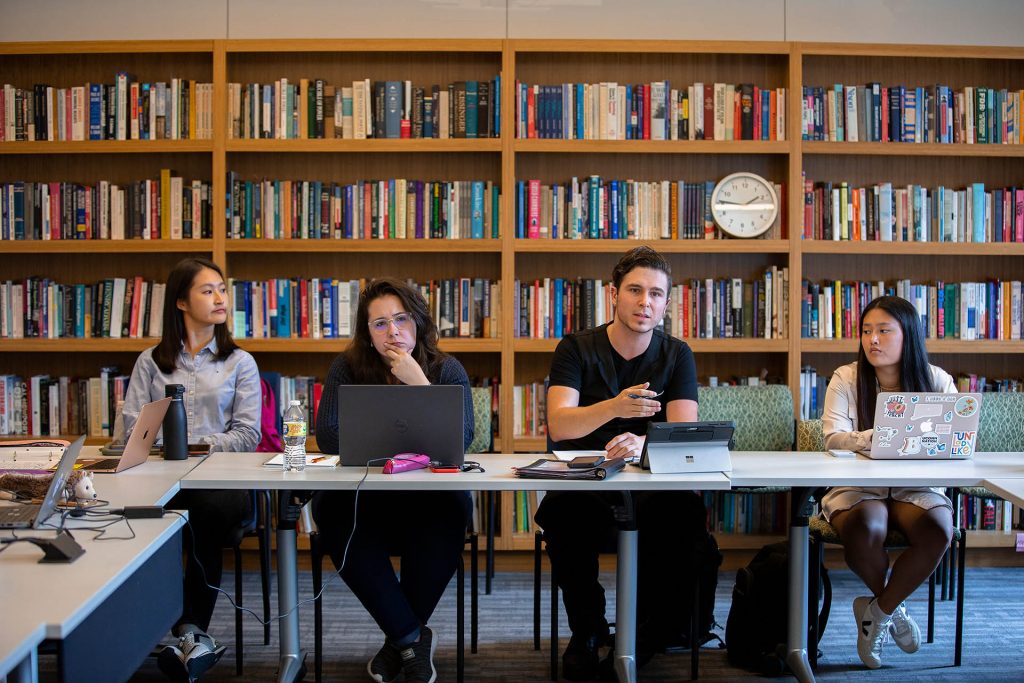 Four students sit in front of full book cases in a graduate seminar